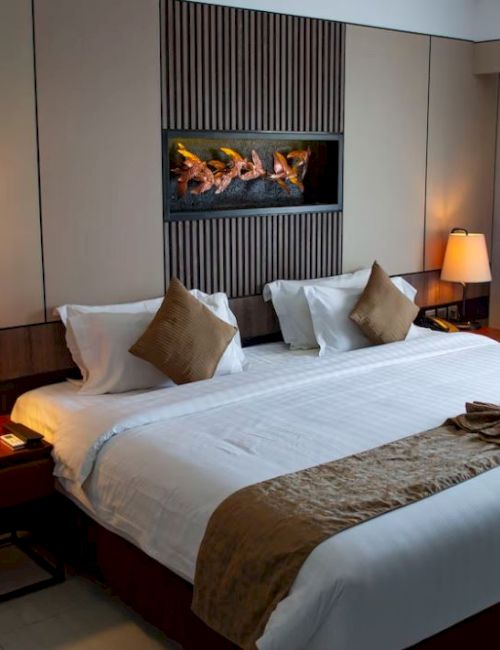 A cozy hotel room with a large bed, decorative pillows, lamps on side tables, and a modern wall feature above the headboard.