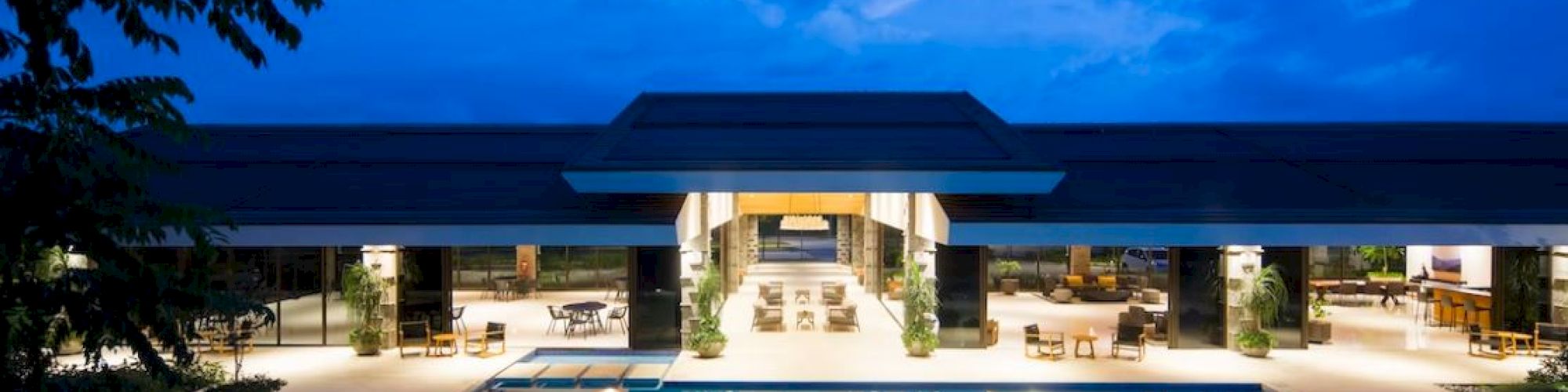 A luxurious modern building with a large illuminated pool at night, surrounded by seating and a vibrant sky overhead.