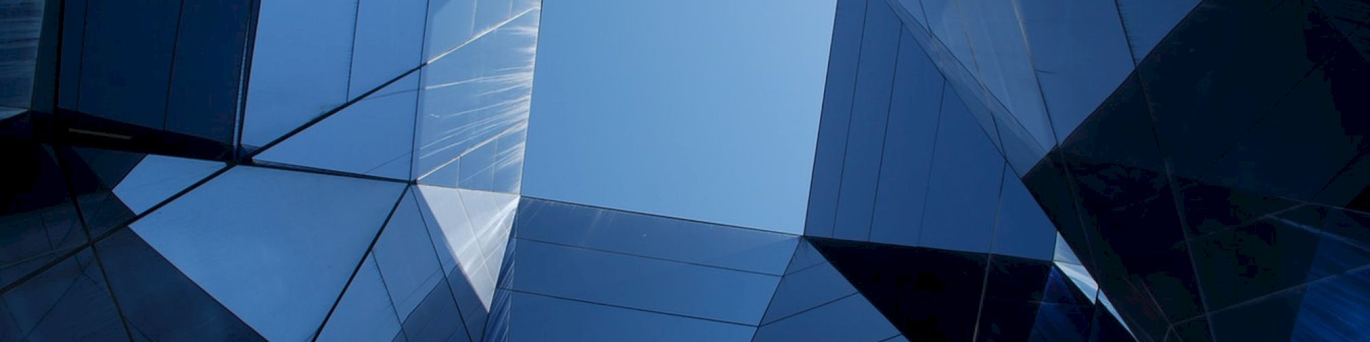 A view upwards through reflective glass buildings forms a geometric pattern with the sky visible at the top center.
