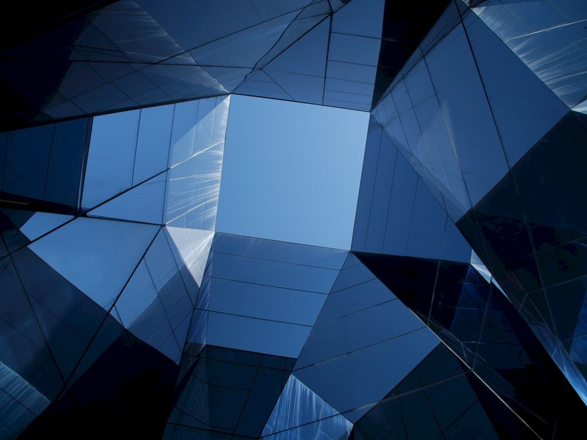 The image shows a view looking up at a group of mirrored buildings reflecting the sky, creating a geometric pattern.