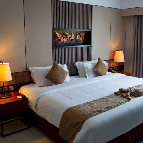 A cozy hotel room with a large bed, decorative pillows, bedside lamps, and curtains, creating a warm and inviting atmosphere.