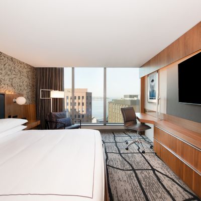 A modern hotel room with a large bed, desk, chair, TV, and cityscape view through a window, decorated with a patterned wall and cozy lighting.