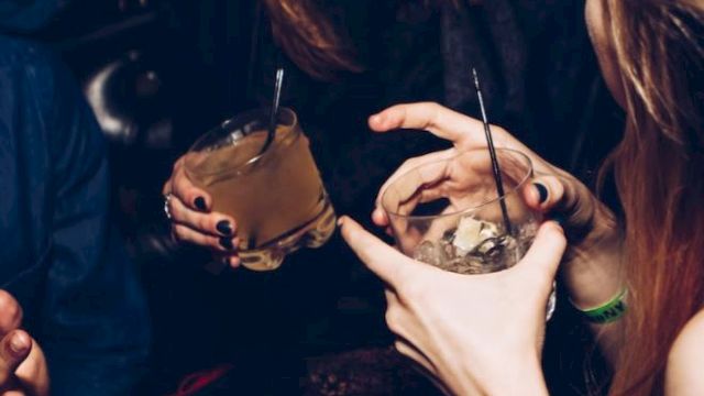 People are sitting and holding drinks, with one person laughing and others engaging in conversation in a social setting.