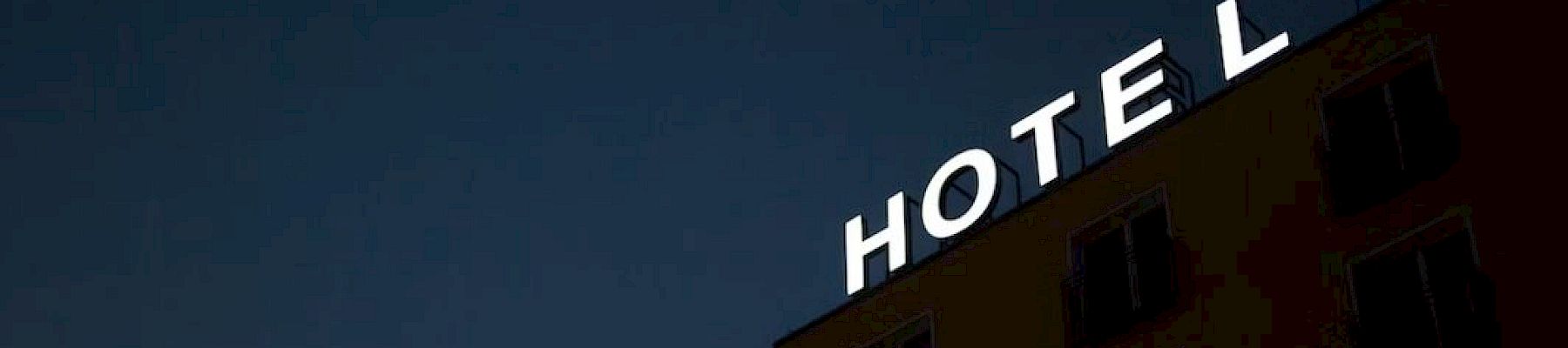 A building with a partially lit "HOTEL" sign against a dark sky; the letter "L" is obscured, suggesting a missing or broken light.