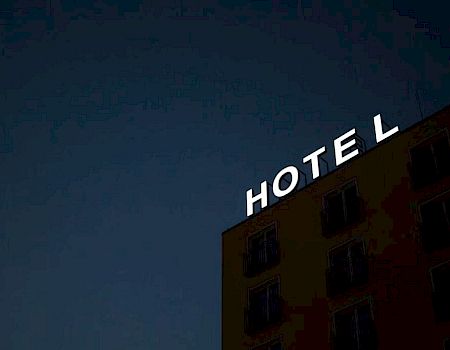A building with a partially lit "HOTEL" sign against a dark sky; the letter "L" is obscured, suggesting a missing or broken light.
