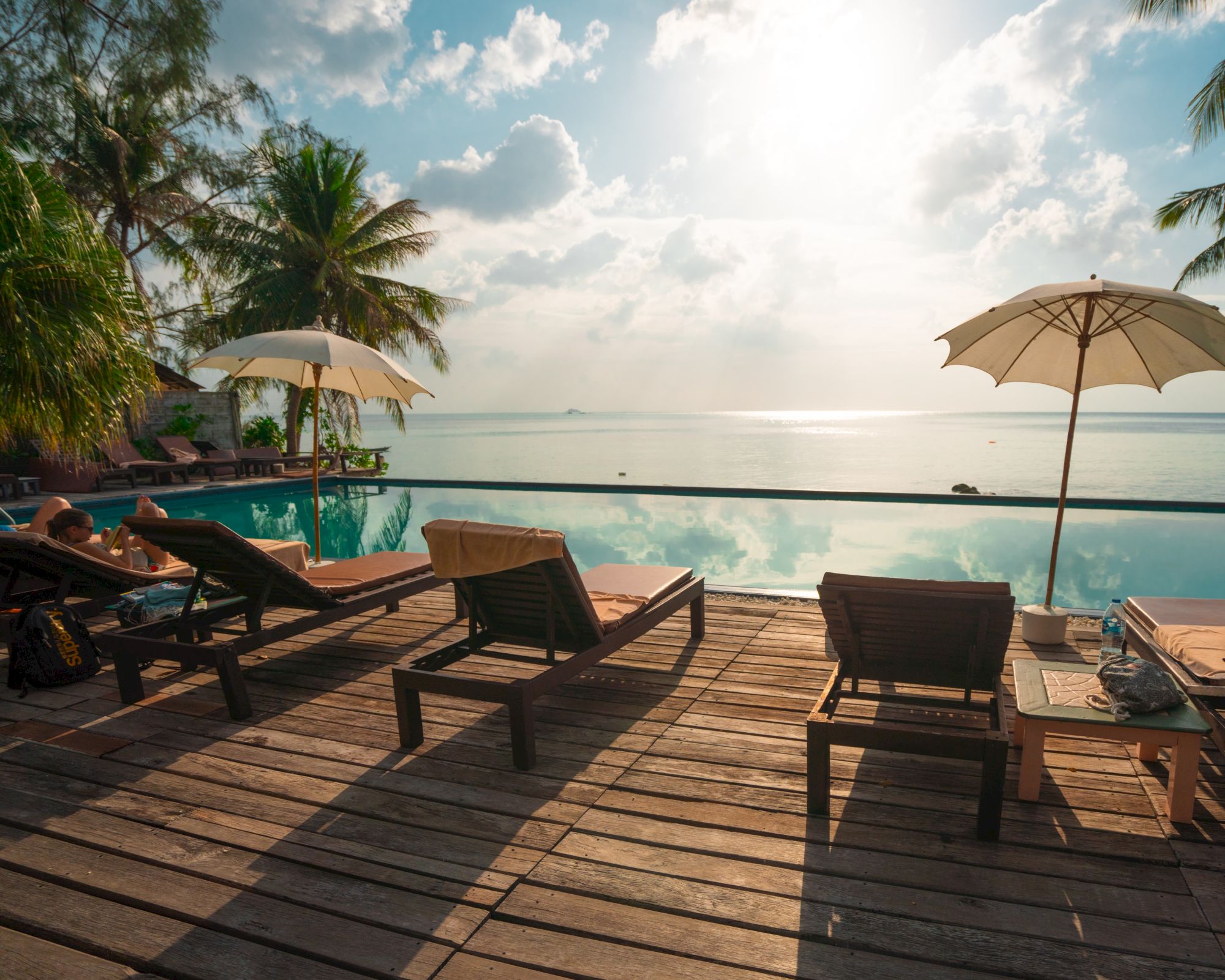 Poolside scene with loungers, umbrellas, and a view of the ocean under a bright sky.
