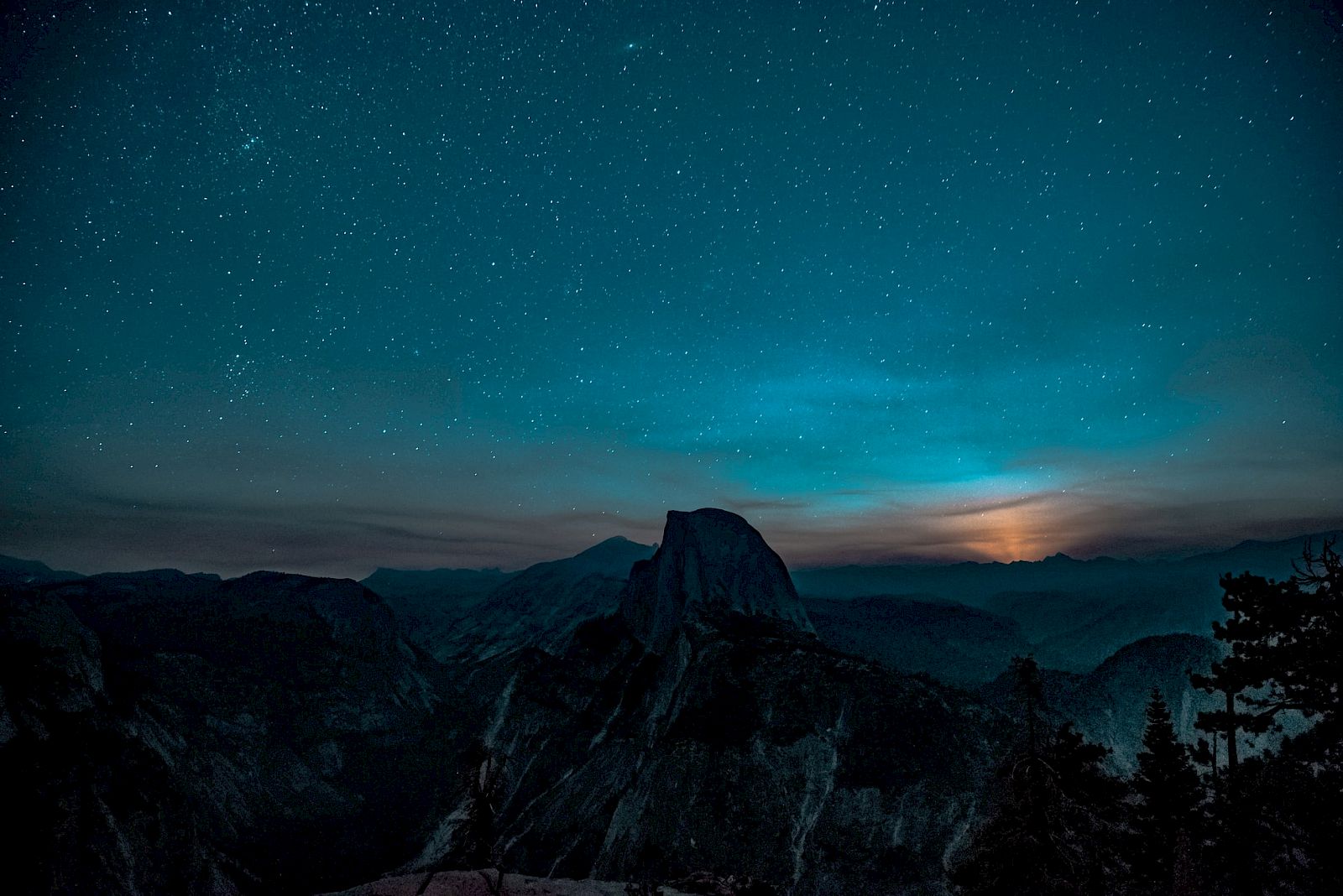 A starry night sky over a mountainous landscape with the moon peeking above the horizon, creating a serene and mystical scene.