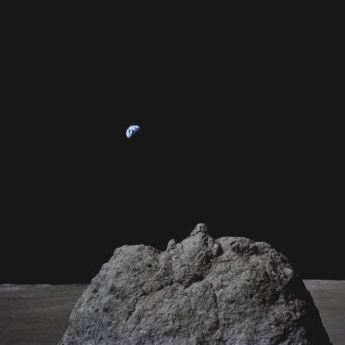 A rocky lunar surface with Earth visible in the distant black sky, creating a dramatic scene from space in the image.