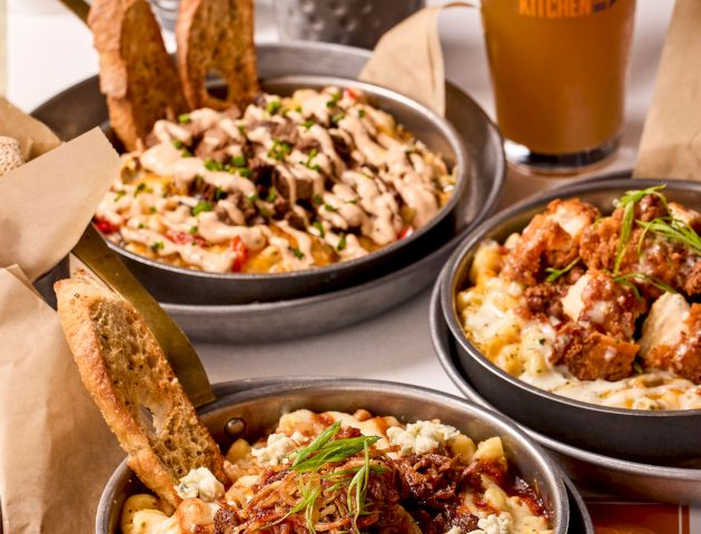 Bowls of comfort food with various toppings, glasses of beer, a basket of bread, and salt pepper shakers in the background.