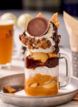 A decadent dessert in a jar with layers of cake, whipped cream, chocolate sauce, peanut butter cup, and garnishes.