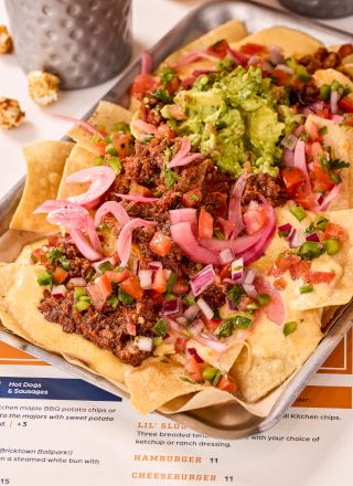 A tray of nachos topped with ground beef, guacamole, diced onions, tomatoes, and jalapeños.