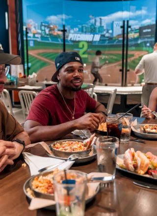 People sitting around a table in a restaurant, enjoying a meal with plates of food, such as pizza and sandwiches, and drinks.
