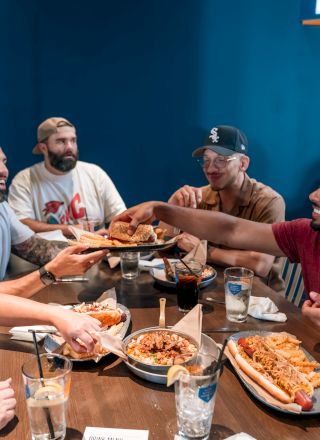 A group of people sitting around a table, sharing food and drinks, with a lively and friendly atmosphere in a casual setting.