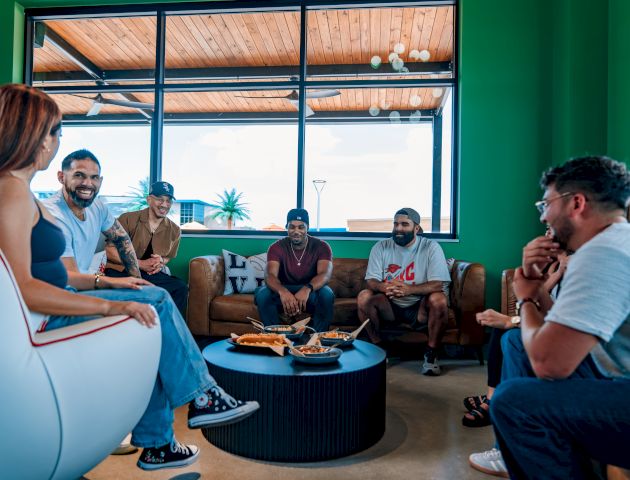 A group of people are sitting in a circle in a room with green walls, engaged in conversation.