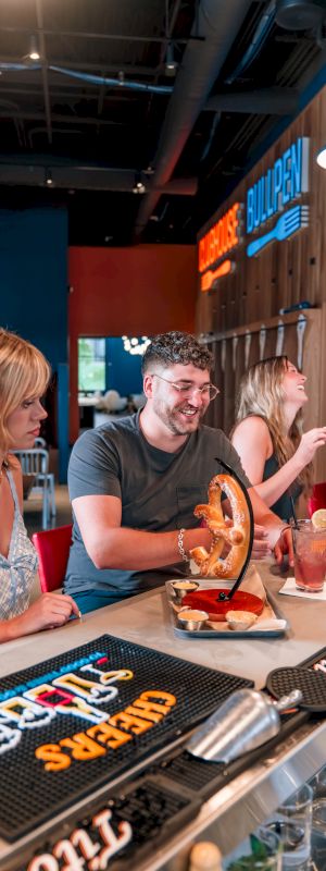 A group of people enjoying drinks and food at a bar, with a man holding a large pretzel.
