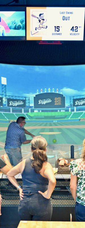 People are playing a baseball simulation game in a venue with big screens and sports-themed decor.
