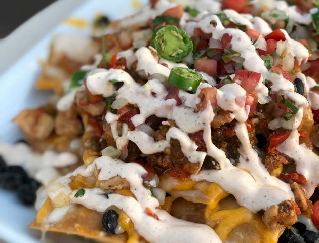 A plate of nachos topped with cheese, pico de gallo, jalapeños, and a drizzle of creamy sauce.