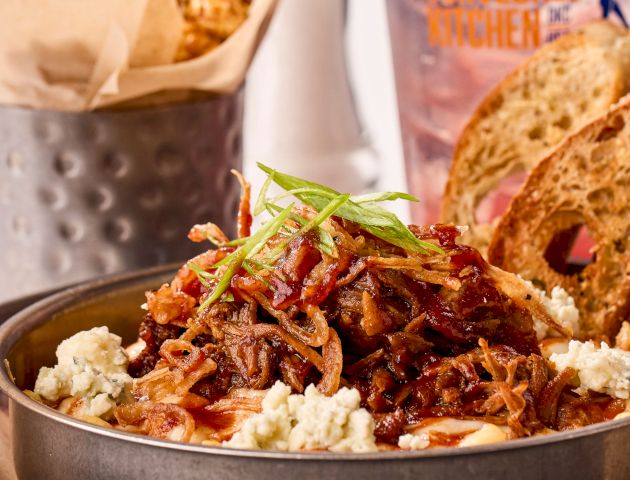 A dish with pulled pork, crumbled cheese, and crispy onions, garnished with green onions, served with toasted bread slices.