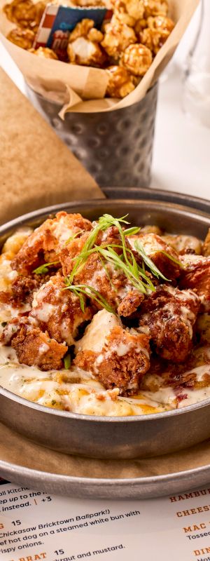 A dish of creamy pasta topped with fried chicken and greens, served with bread slices, next to a cup of caramel popcorn and a drink.