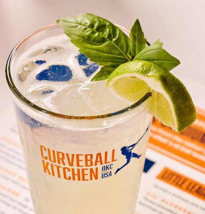 A refreshing drink in a "Curveball Kitchen" glass, garnished with lime and basil leaves, placed on a menu.