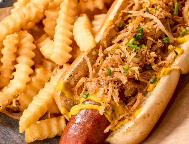 A hot dog topped with crispy onions and chives, served with crinkle-cut fries on the side.