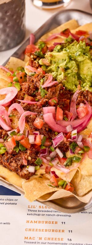 A tray of nachos topped with ground meat, guacamole, cheese, diced tomatoes, pickled onions, and jalapeños.