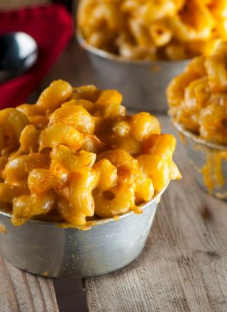 Three bowls of cheesy macaroni sit on a wooden surface with a red cloth and a spoon nearby.
