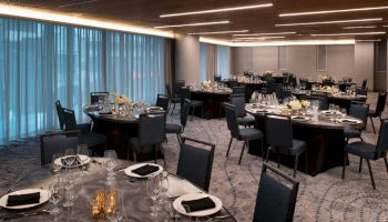 A well-set banquet hall with round tables, chairs, and tableware, featuring floral centerpieces and dim lighting.