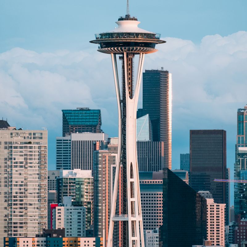The image shows the Space Needle in Seattle with a backdrop of skyscrapers under a blue sky with clouds.
