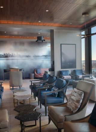 A modern lounge with leather chairs, small tables, and large windows showing a waterfront view with a Ferris wheel.