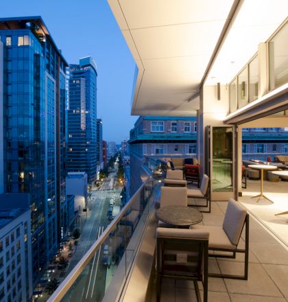 A modern cityscape with high-rise buildings and a sleek balcony showcasing outdoor seating, all under a twilight sky.