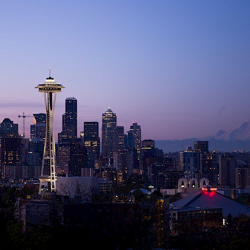 A twilight view of Seattle's skyline with the Space Needle, high-rise buildings, and Mount Rainier in the background.