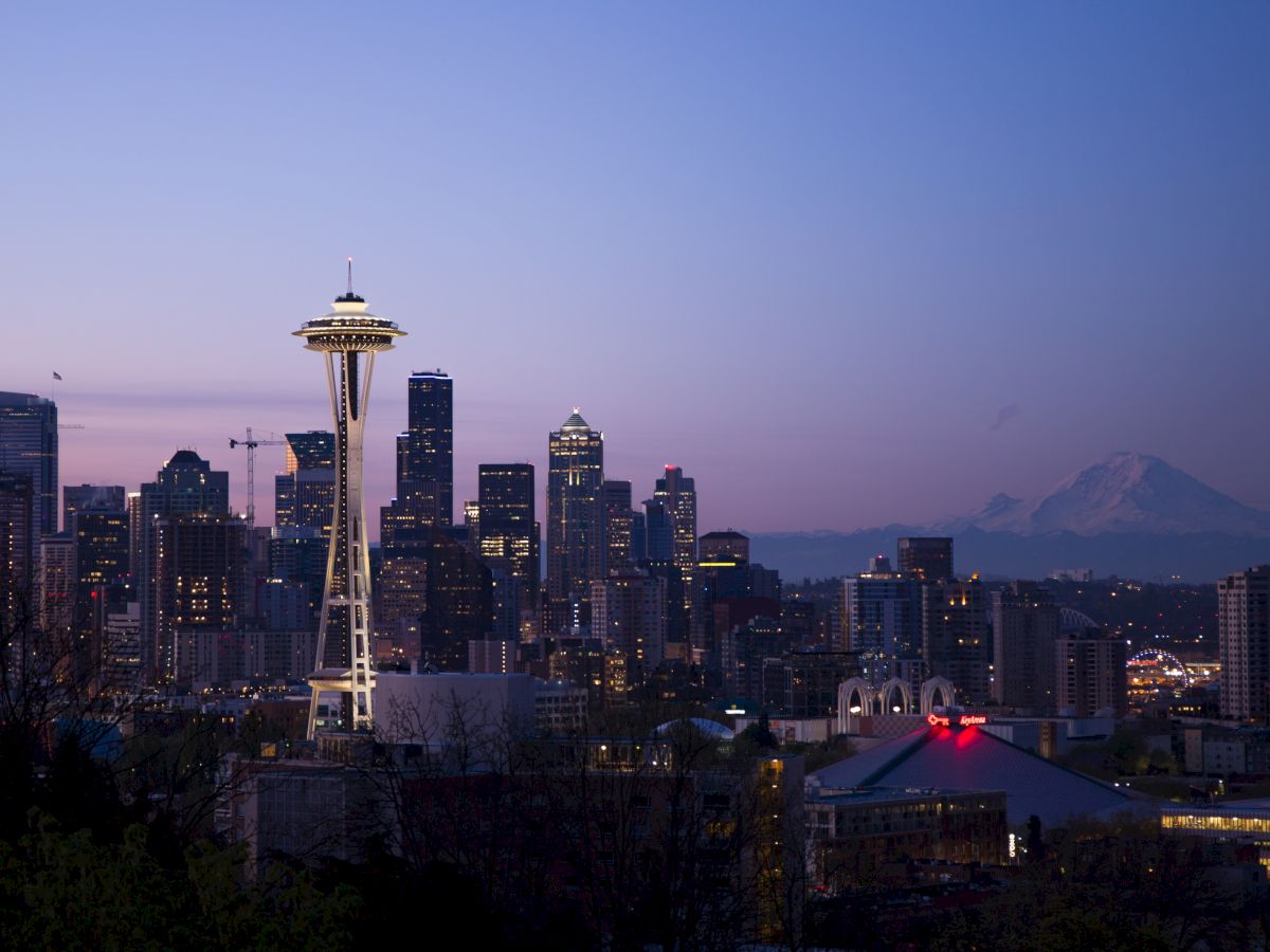 Seattle skyline featuring the Space Needle at dusk with Mount Rainier in the background, under a clear, evening sky.