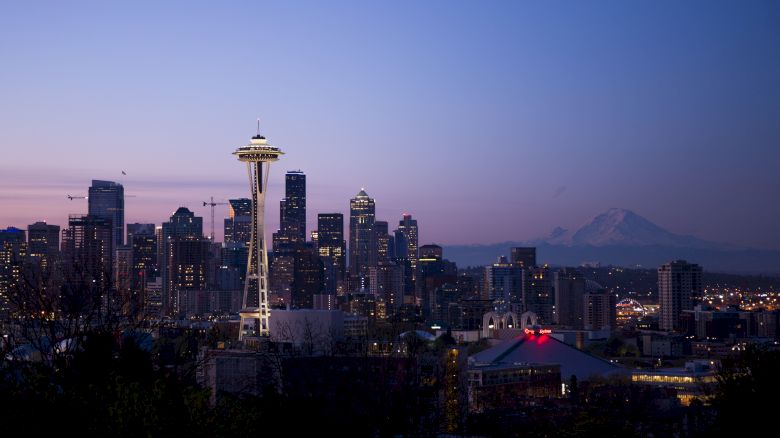 Seattle skyline featuring the Space Needle at dusk with Mount Rainier in the background, under a clear, evening sky.