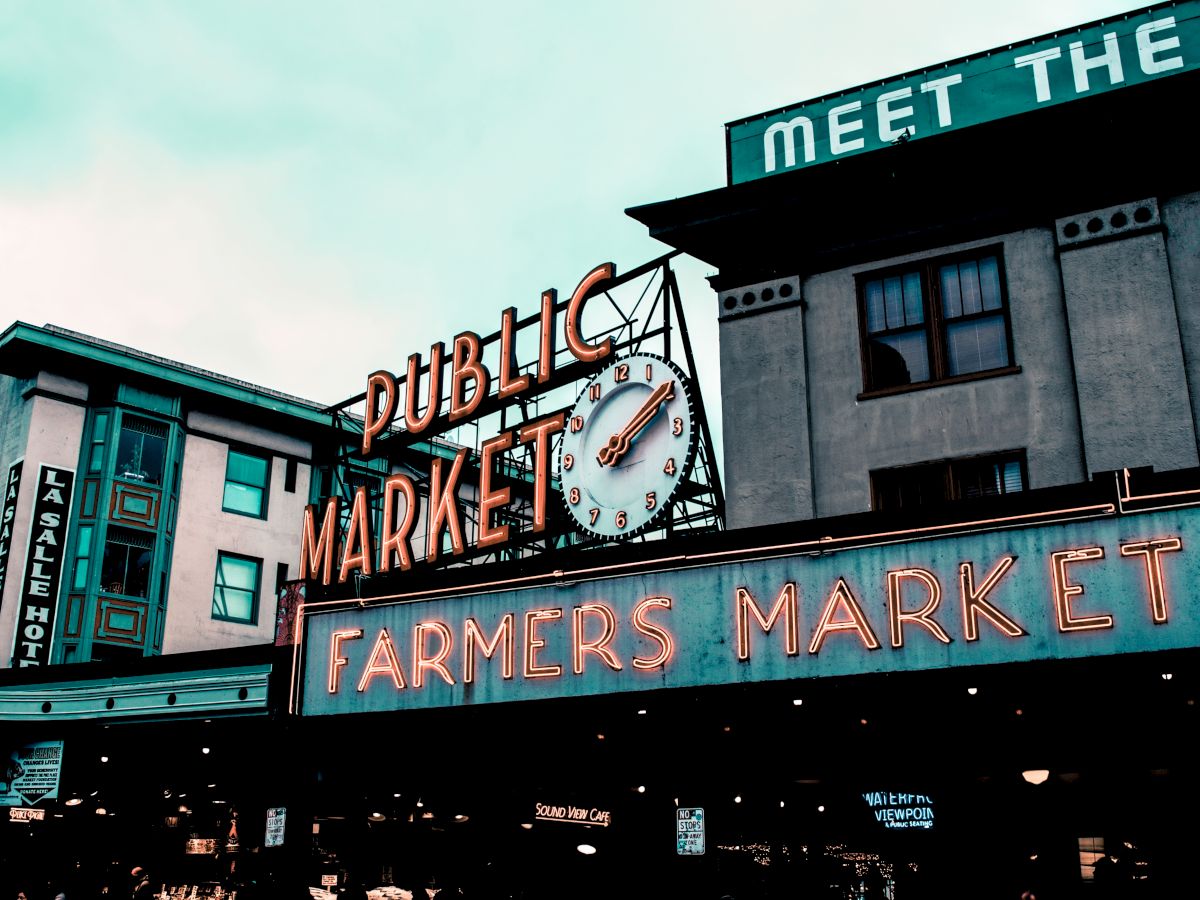 The image shows the iconic Public Market sign with a clock, and the Farmers Market sign at Pike Place Market in Seattle.